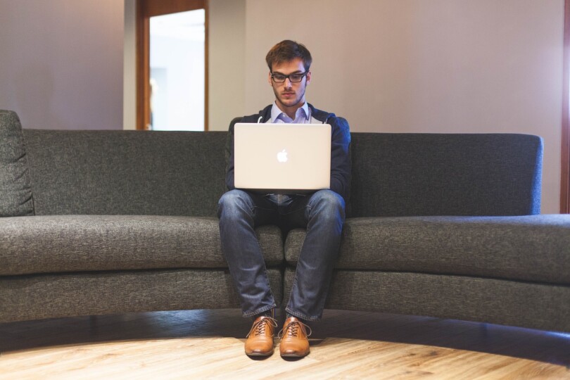 Un homme assis sur un canapé qui regarde un ordinateur portable
