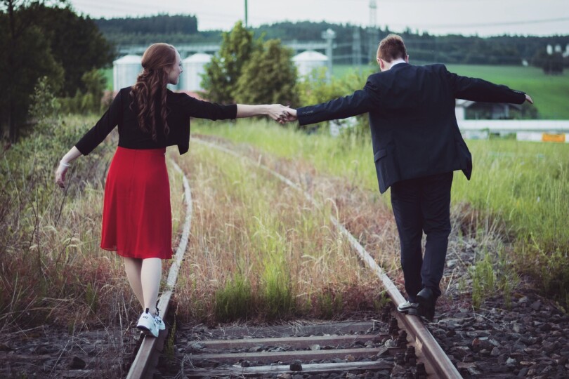 Un homme et une femme qui se tienne la main tout en marchant chacun de leur coter sur les rails d’un chemin de fer, confiance relation platonique