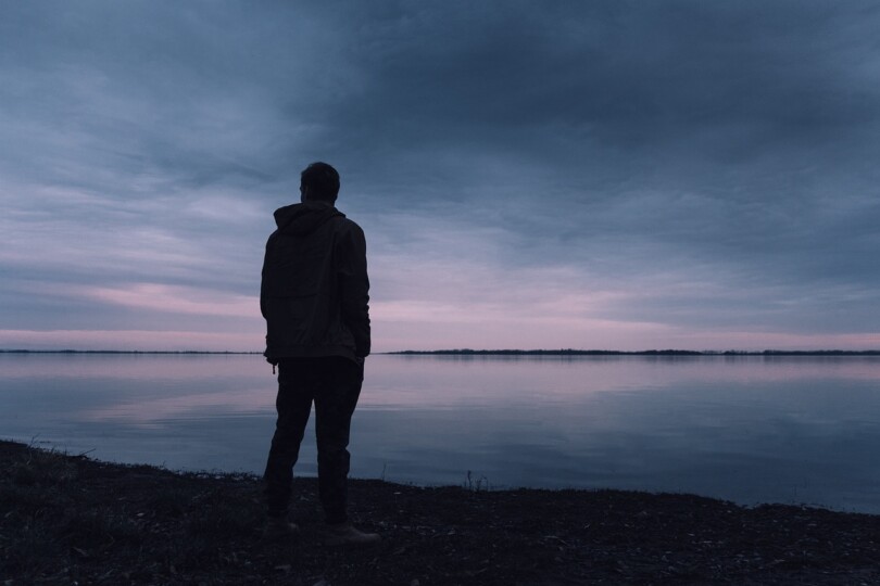 Un homme solitaire de dos au bord d’un lac qui regarde au loin