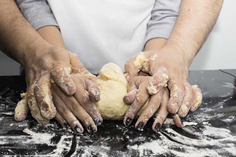 Zoom sur les mains d’un chef pâtissier qui tienne les mains de son élève pour lui montrer comment pétrir la pâte