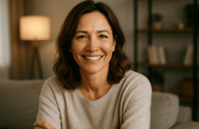 Photo réaliste d’une femme souriante d’une quarantaine d’années, cheveux bruns mi-longs, assise dans un salon moderne et lumineux, incarnant confiance et sérénité.