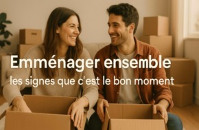 Photo d’un couple souriant assis parmi des cartons de déménagement, symbolisant l’emménagement ensemble et les signes que c’est le bon moment.