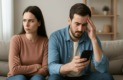 couple assis sur un canapé montrant des signes de tension et de jalousie, la femme contrariée et l’homme absorbé par son téléphone