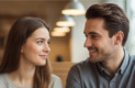 Cette photographie capture un moment clé d'une interaction respectueuse et douce entre un jeune homme et une jeune femme dans un environnement de café paisible. Le couple se regarde avec des sourires subtils et complices, évoquant une connexion authentique et un intérêt mutuel naissant. La femme, avec une expression légèrement réservée mais engageante, reflète la thématique de la timidité, tandis que l'homme témoigne de patience et de compréhension. L'arrière-plan du café, lumineux et chaleureux, avec ses boiseries claires et ses luminaires doux, suggère un cadre idéal et non intimidant pour une première rencontre ou une conversation approfondie. L'image illustre parfaitement les principes de communication non verbale et de construction de confiance abordés dans l'article sur comment aborder une femme timide, soulignant l'importance de l'écoute et du respect dans le processus de séduction.