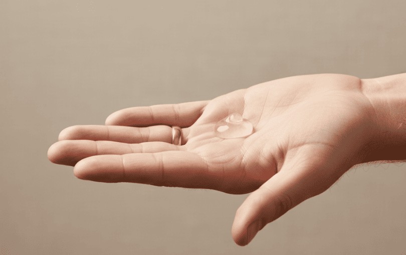 Main masculine appliquant du lubrifiant avec geste délicat sur fond sobre et élégant